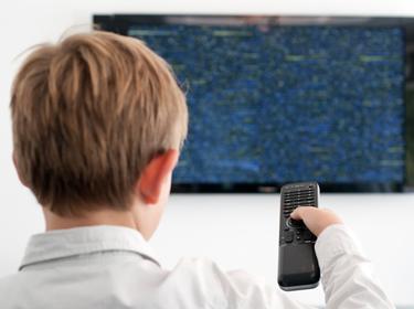 A boy points a remote control at a television