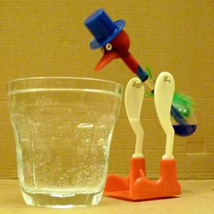 A drinking bird toy next to a glass of water