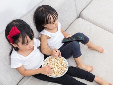 Two girls on a couch watching TV while eating popcorn