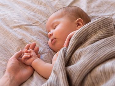 Sleeping baby with adult hand holding baby's hand, photo by Amax Photo/Getty Images