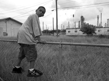 A boy in the Hillcrest section of Corpus Christi, Texas, at the fence line of a refinery in August 2007, photo by Peter Essick/Cavan Images/Alamy
