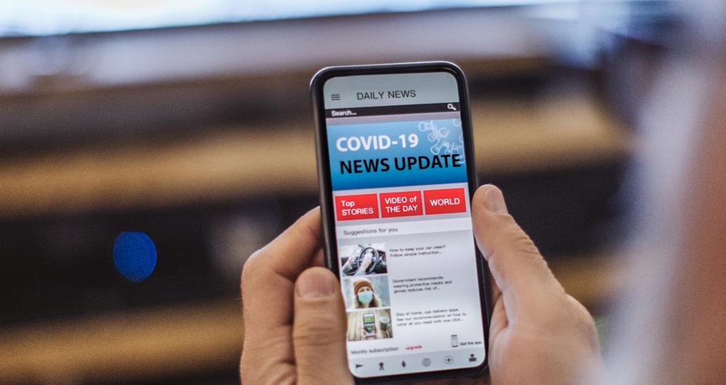 A person looks at a COVID-19 news update on their cell phone, photo by svetikd/Getty Images