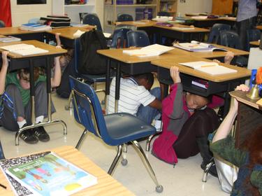 Students participate in the Great Southeast ShakeOut earthquake drill at Langston Hughes Middle School in Reston, Virginia. They are conducting the "drop, cover and hold on" safety procedure.