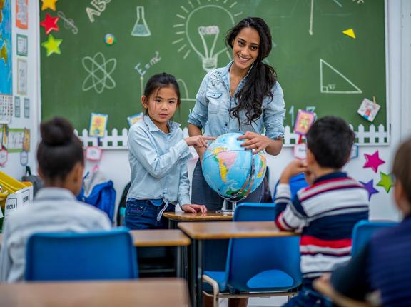 A student giving a presentation to her class points at a globe next to her teacher, photo by FatCamera/Getty Images