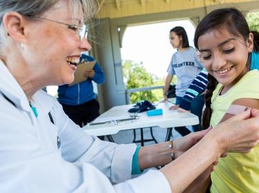 Cheerful doctor places adhesive bandage on preteen girl's arm, photo by SDI Productions/Getty Images