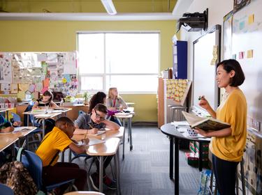 Asian teacher standing at the front of a middle school classroom teaching students, photo by Hero Images/Getty Images