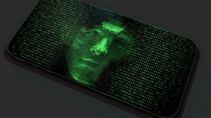 Green face peering out of machine code on cell phone, photo by Devrimb/Getty Images